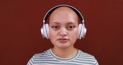 Glatze junge Frau schaut in die Kamera, während sie Musik-Playlist mit kabellosem Kopfhörer hört