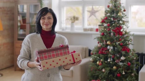 Woman Holding Gifts by Christmas Tree at Home