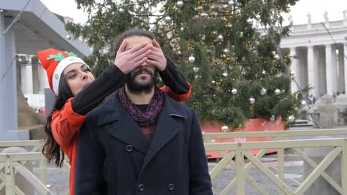 Playful Couple Embracing Near Christmas Tree in City