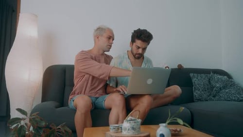 Two Men Using Laptop on Couch at Home