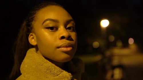 A Young Black Woman Looks Seriously at the Camera in a City Park at Night Face Closeup
