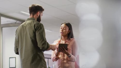 Video of diverse businesswoman and businessman using tablet and talking in office