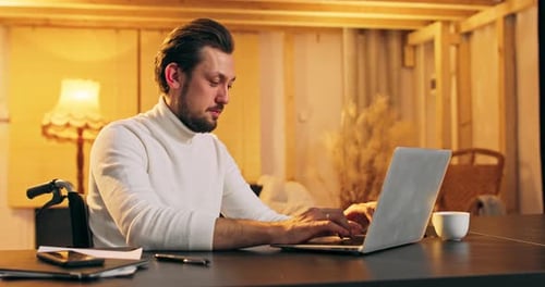 Man in Wheelchair Using Laptop in Home at Night