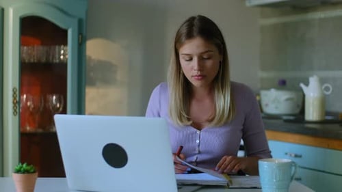 Woman Working at Laptop and Writing in Notebook
