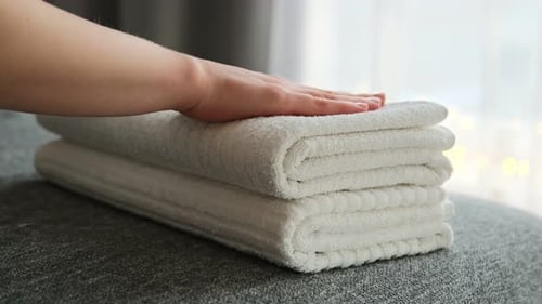 Frauenhände legen Stapel frischer, sauberer weißer Badetücher auf das Bett.