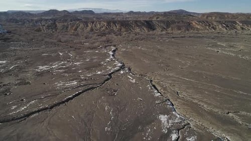 Flying from over top of snow stripped dune towards winding river