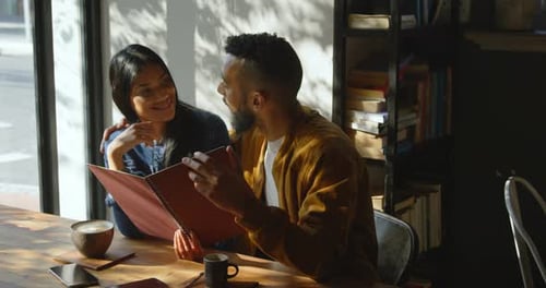 Front view of young mixed-race couple discussing over menu card in cafe 4k