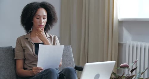 Woman Reviews Documents While Sitting Indoors with Laptop