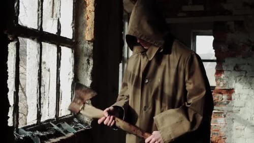 a Man in a Long Cloak with a Hood Walks in an Abandoned Building with Bloody Ax