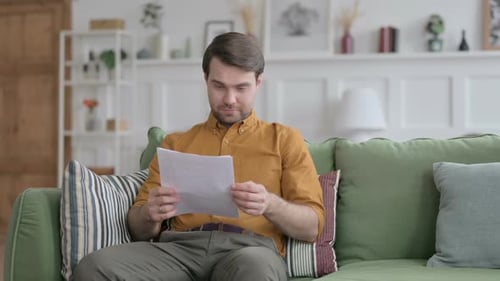 Man Reading Good News on Couch at Home