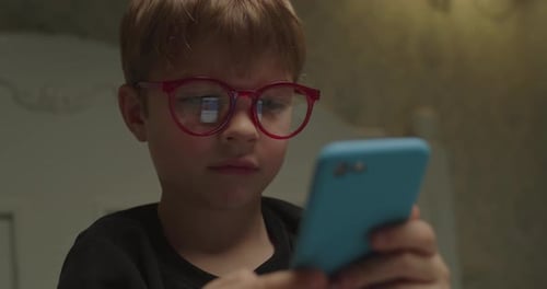 Child Wearing Glasses Uses a Phone Indoors
