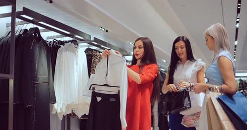 Girl Chooses Clothes and a Woman's Handbag in the Store and Consults with Her Friends