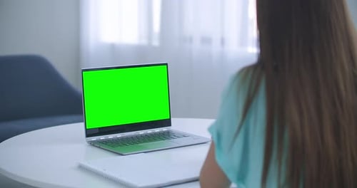 Girl Taking Notes in Notepad From Laptop Computer Green Mockup Screen. Girl Learning Online on