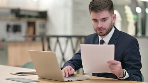 Businessman Working on Laptop with Documents in Office