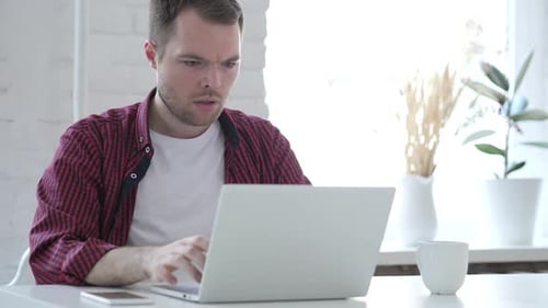 Junger Mann unter Schock bei der Arbeit am Laptop