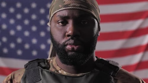 Man in Military Gear Stands in Front of US Flag