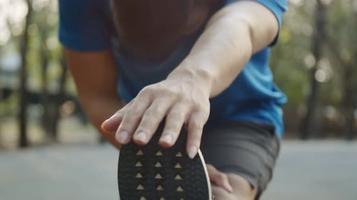 Handheld shot athletic man doing leg stretch warming before exercises at the park.