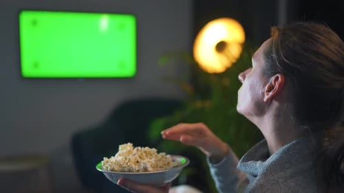 Woman Sitting on a Sofa in the Living Room in the Evening and Watching a Green TV Screen Mockup
