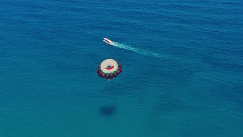 Aerial View. People Flying on a Colorful Parachute Towed By a Motor Boat. Parasailing in Blue Sky.
