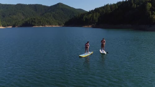 Aerial drone shot of couple paddling stand up paddle boards on lake