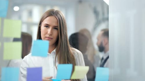 Pensive Beautiful Businesswoman Working with Colored Sticky Notes Looking at Glass Board