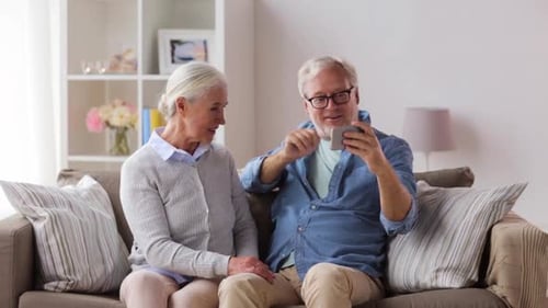 Mature Couple Smile and Use Phone on Couch