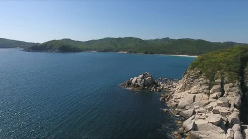 Aerial Shot Moving Along the Coastline of Deep Blue Sea Along a Dramatic Cliff Edge on Sunny Day