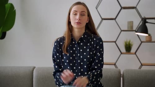 Junge glückliche kaukasische Frau spricht, während sie in die Kamera schaut, während sie auf dem Sofa in der
