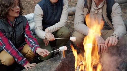Happy Young Family Roasting and Eating Marshmallow Outdoors in Autumn Forest