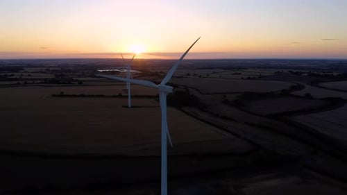 Large wind turbines with blades in field aerial view bright orange sunset.