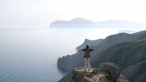 Young Woman Raises Her Hands Up Standing on the Top of a Mountain