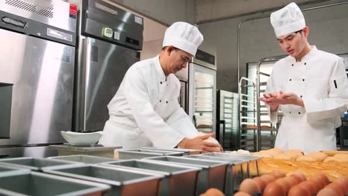 Asian male chefs in uniforms are preparing to bake bread in a stainless kitchen.
