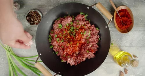 Hand adding salt to ground meat in wok