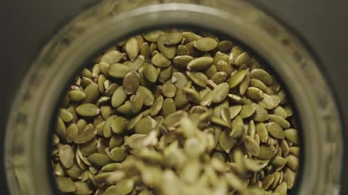 TOP VIEW: Peeled Pumpkin Seeds Fall Into Glass Jar - Slow Motion