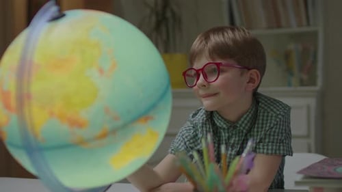 Boy Wearing Glasses Exploring Globe at Desk