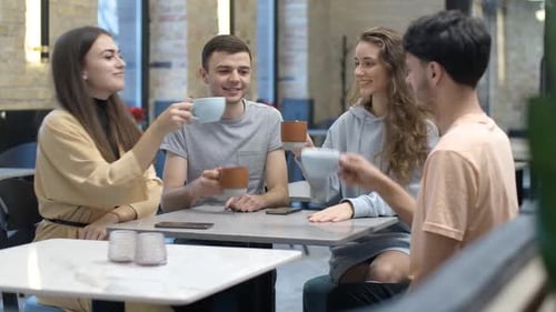 Positive Young Woman Toasting and Clinking Coffee Cups with Friends in Cafe
