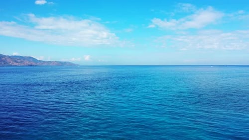 Blue seascape with endless sea reflecting bright sky of sunrise with overhanging white clouds in Ind