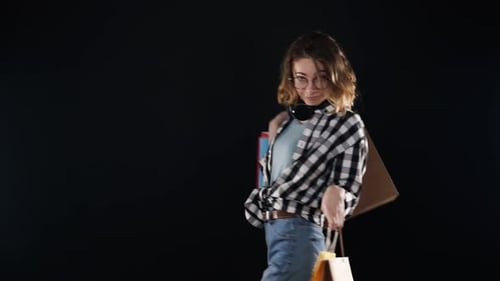 Belle femme souriante en chemise à carreaux et jeans marchant joyeusement avec des sacs à provisions colorés