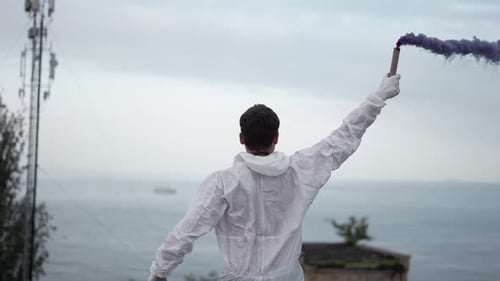 Homme en costume de protection debout sur le bord du toit avec un bâton de fumée bleu