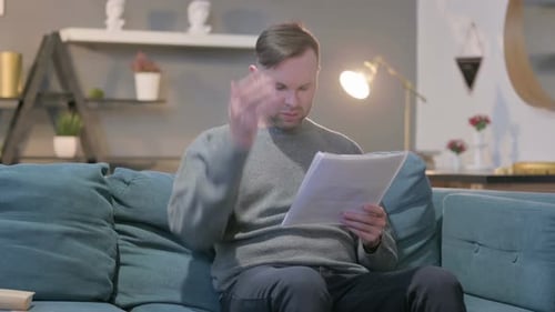 Worried Man Reads Documents on Couch at Home