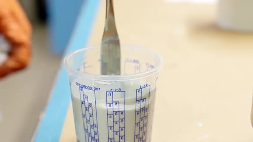 Nahaufnahme des Eingießens hellblauer Farbe in den Messbecher