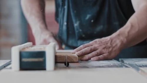 Carpentry Works Worker Slowly Cutting the Long Wooden Detail in Two Single Parts Using an Automatic