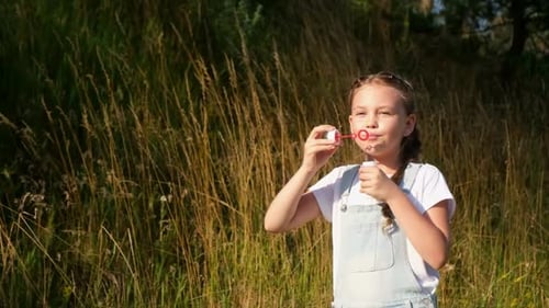 Girl Blowing Bubbles in Grassy Field on Summer Day