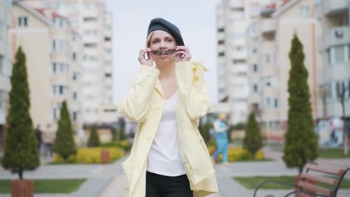 Stylish Woman Walks in Urban Park, Removes Sunglasses