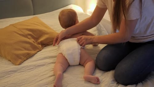 Mother Changes Infant's Diaper on Bed