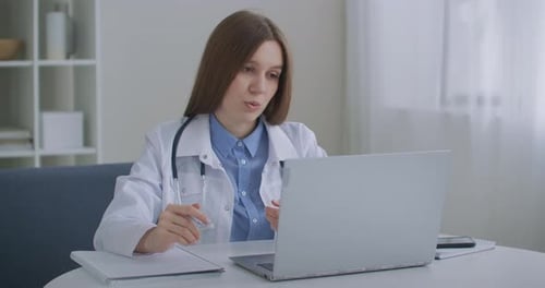 Doctor Consults Online, Takes Notes at Desk