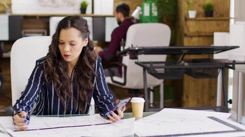 Architect Working on Plans with Smartphone in Office