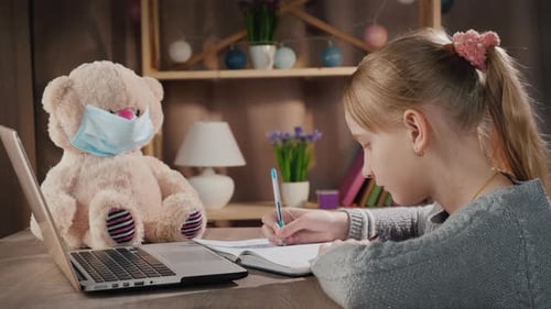School Online Pupil Doing Lessons Near Laptop Next to a Teddy Bear in a Protective Mask