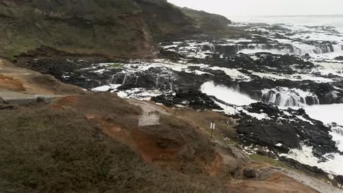Slowly tracking forward as twin waves crash upon a jagged rocky shore, aerial