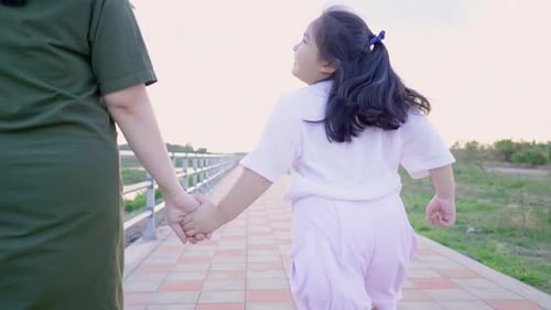 Back view of Asian mom and kid holding hand and running outdoor